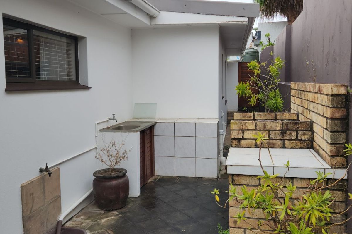 A functional rear exterior utility area featuring a built-in brick braai or prep station, tiled surfaces, and a wall-mounted outdoor tap.