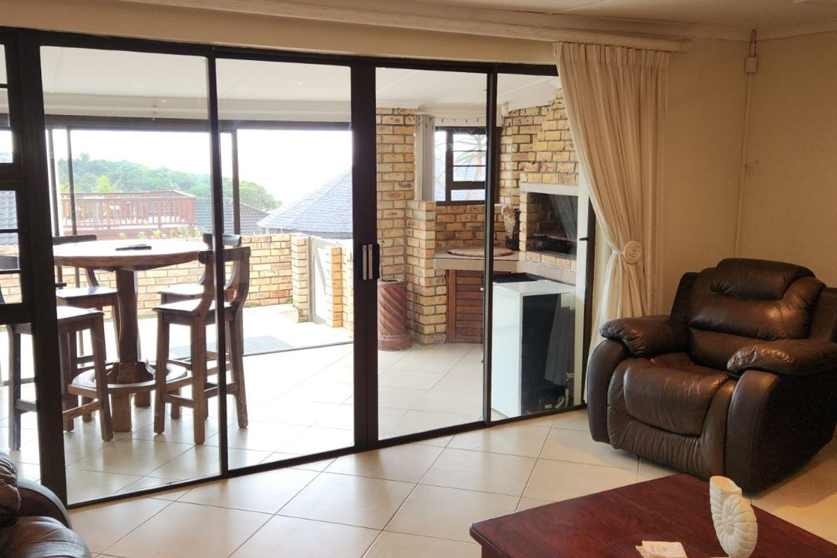 Living room featuring large sliding glass doors that open onto a covered patio with a built-in brick braai area.