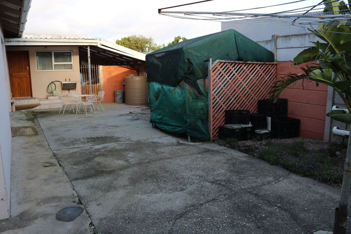 A paved rear courtyard area featuring a covered patio section, a water storage tank, and a utility structure with shade cloth covering.