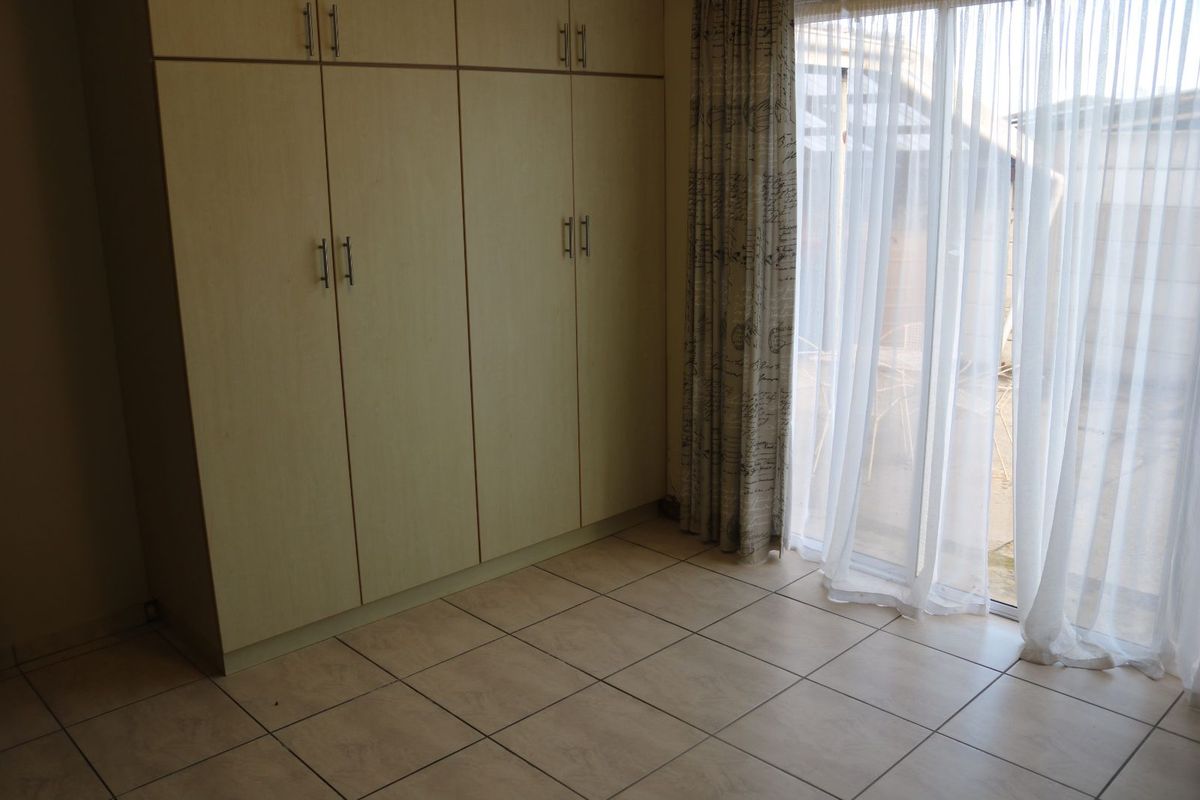 A bedroom featuring built-in cupboards and tiled flooring, with sliding glass doors providing access to the exterior.