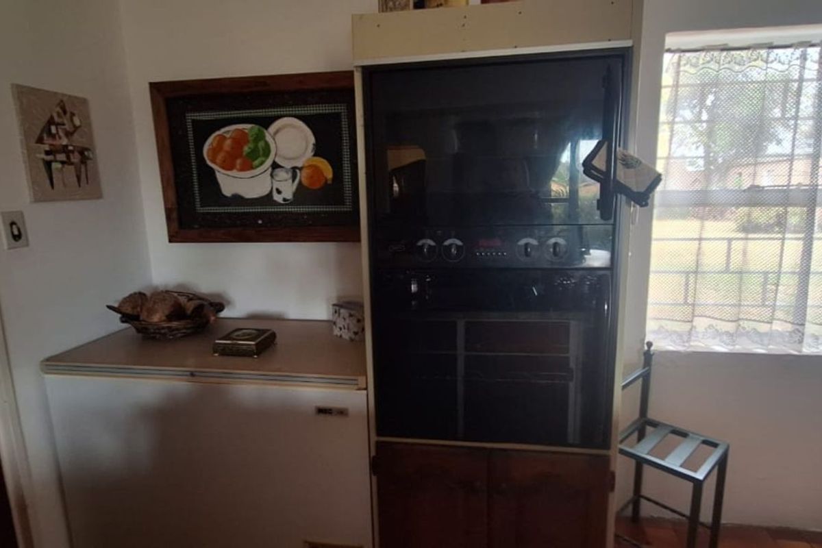 A dated kitchen area featuring a built-in eye-level oven and adjacent counter space with tiled flooring and natural light from a large window.
