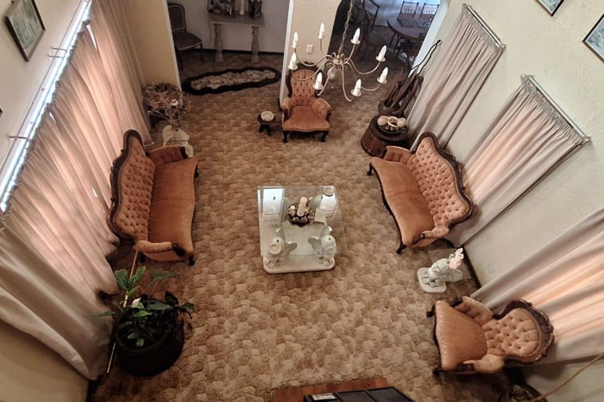 High-ceiling living area featuring a spacious layout, large windows with curtains, and a central chandelier, offering a classic, traditional aesthetic.