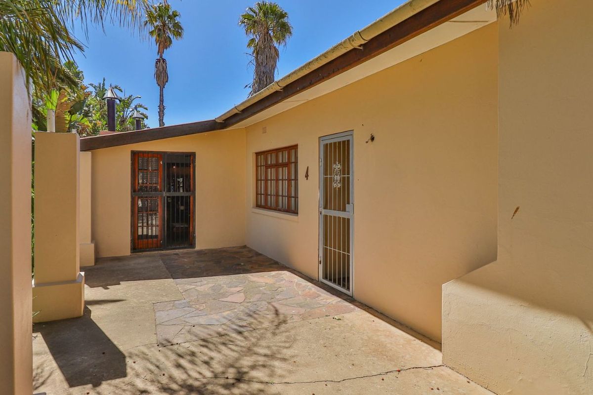 A rear exterior view of the property featuring a paved patio area, security gates, and access to the home.