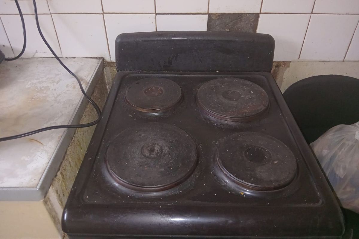 A close-up view of a dated, worn electric stove set against a tiled backsplash with visible signs of wear and damage.