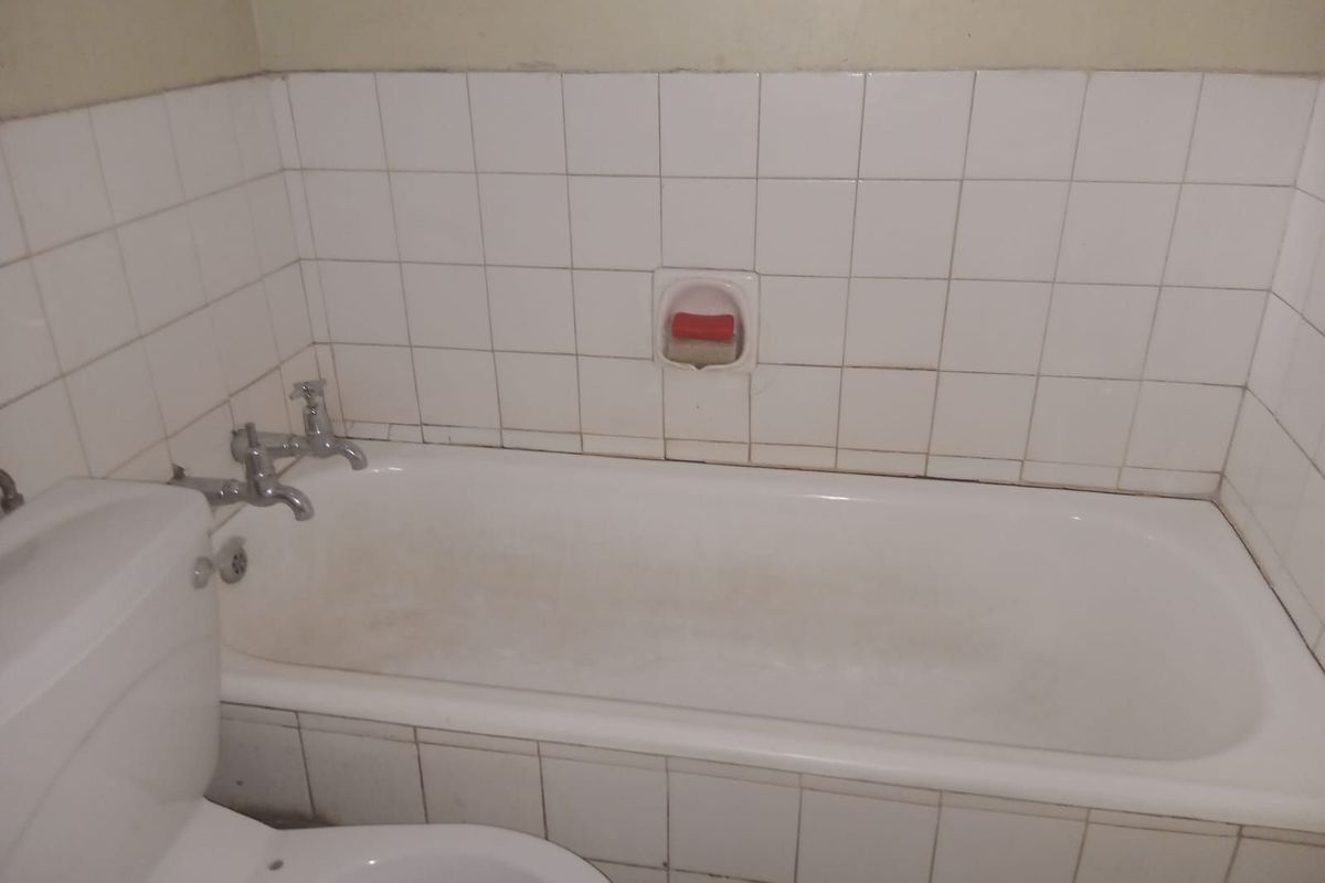 A functional bathroom featuring a standard bathtub with wall-mounted taps and white tiled splashbacks.