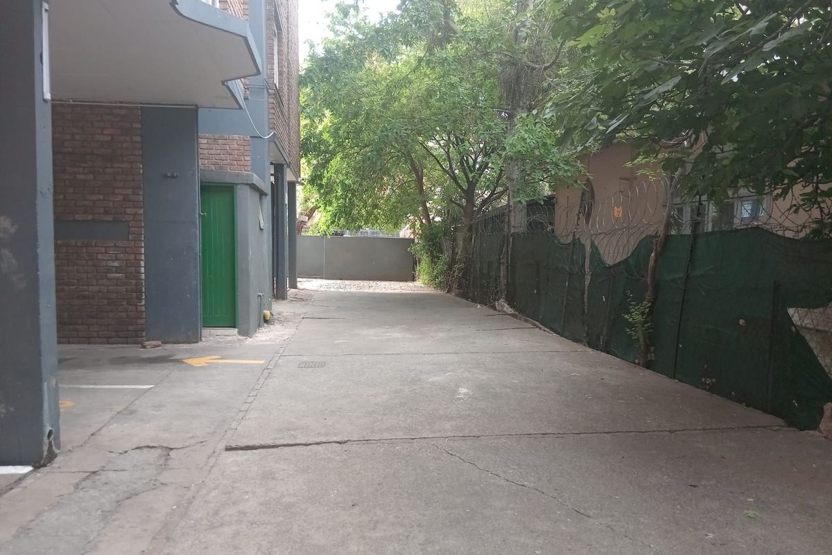 A view of the apartment complex exterior driveway and parking area, featuring concrete paving, brick facade elements, and perimeter fencing.