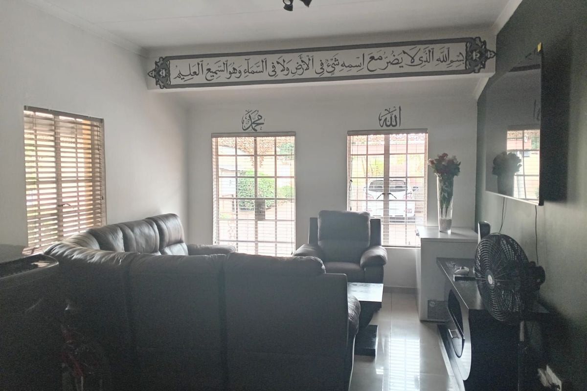 A comfortable living room featuring tiled flooring, large windows with fitted blinds, and a wall-mounted television setup.