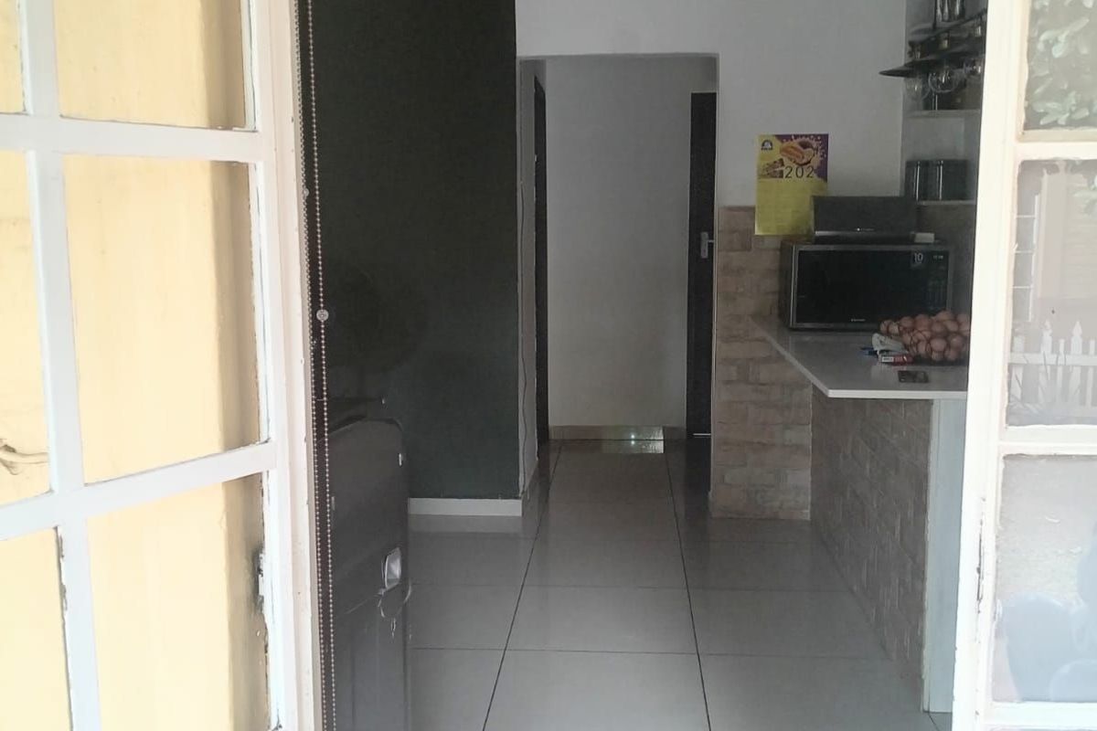 View through a glass-paned door into a tiled kitchen area featuring a breakfast counter and neutral wall finishes.