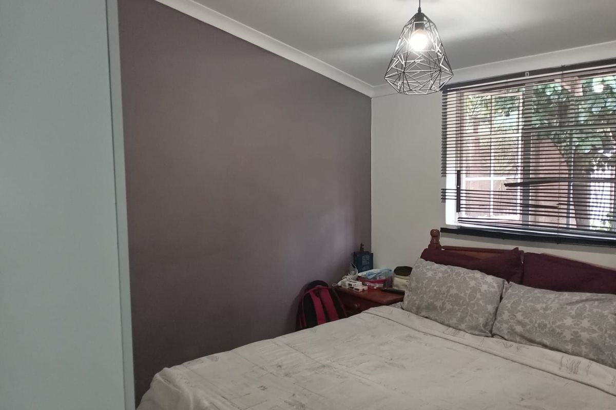 A bedroom featuring a dark accent wall, a window with fitted venetian blinds, and a modern geometric pendant light fixture.