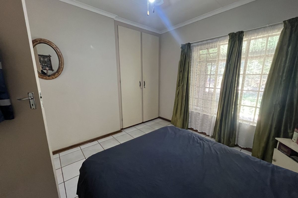 A bedroom featuring tiled flooring, built-in cupboards, and large windows allowing natural light.