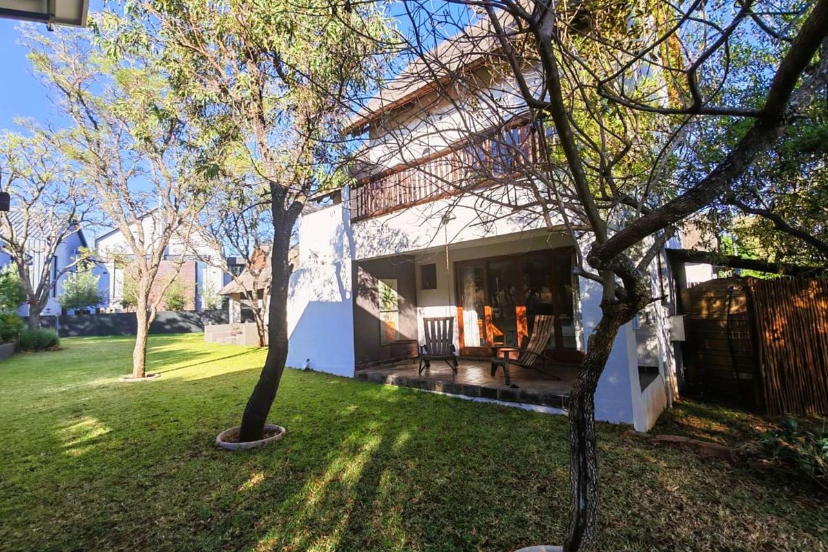 Rear view of the house featuring a covered patio area, a balcony with wooden railings, and a spacious private garden.