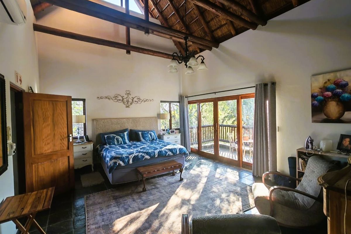 Spacious bedroom featuring a high vaulted thatched ceiling with exposed timber beams, slate flooring, and large sliding doors opening onto a private balcony.