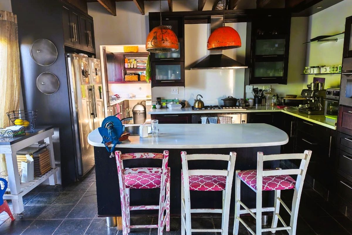 Spacious kitchen featuring dark cabinetry, a central island with stone countertop, exposed timber ceiling beams, and a dedicated scullery area.
