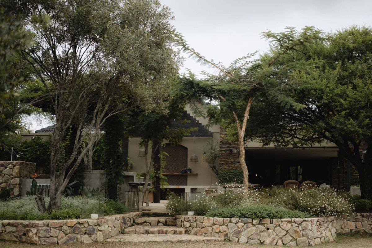 A landscaped rear garden featuring stone retaining walls, mature trees, and a covered patio area with built-in outdoor infrastructure.