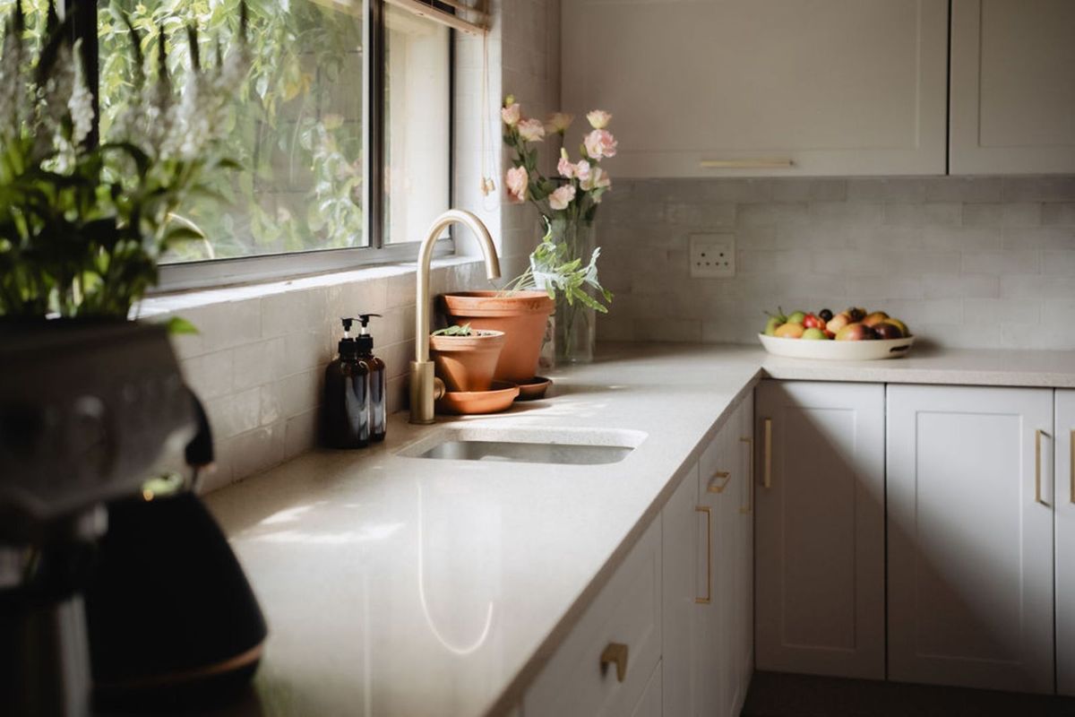 A bright, modern kitchen featuring light-toned cabinetry, stone countertops, a sleek undermount sink, and a stylish brass faucet set against a subway tile backsplash.