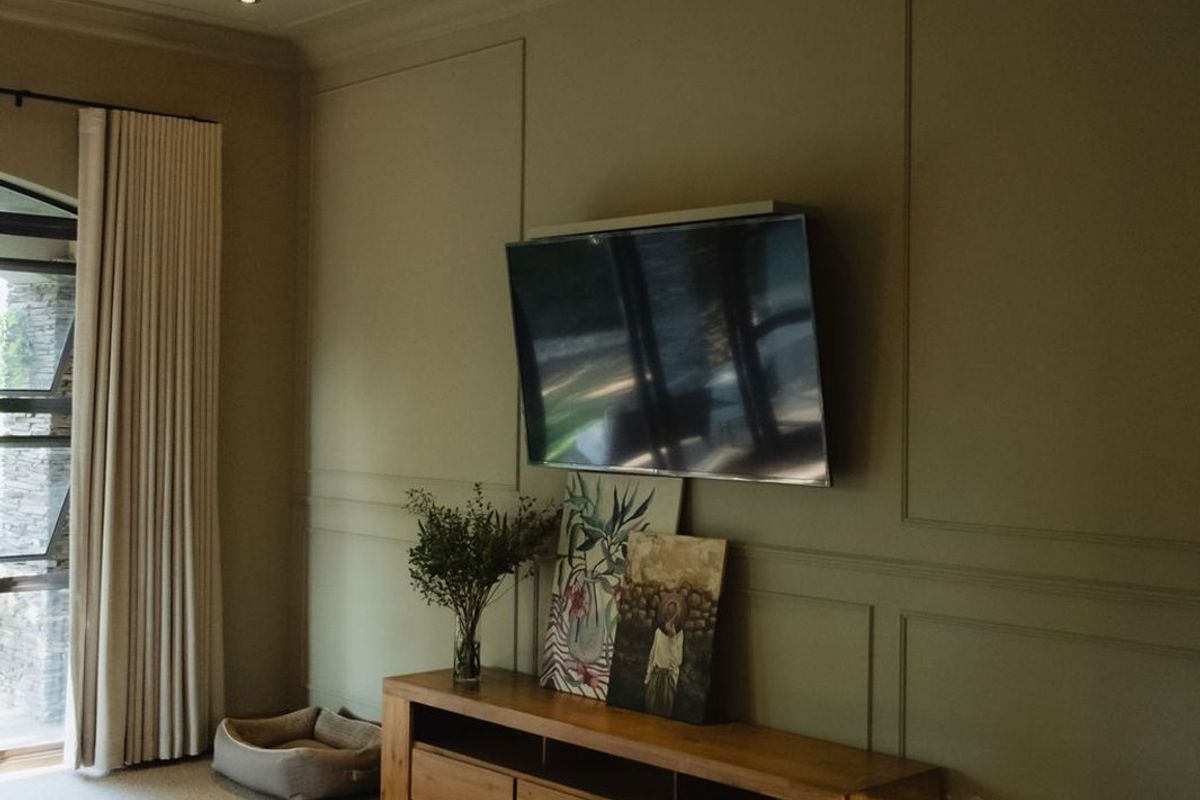 A well-maintained living room featuring elegant wall paneling, recessed ceiling lighting, and large windows with floor-to-ceiling curtains.
