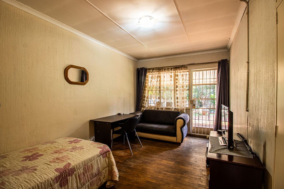 A bedroom featuring parquet flooring, textured walls, and a security gate leading to the exterior, offering a functional layout with natural light.