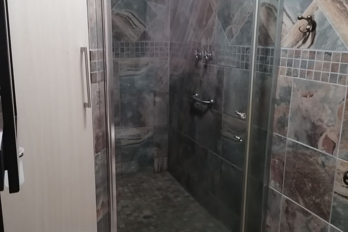 A modern bathroom featuring a walk-in shower with glass enclosure, stone-look wall and floor tiling, and a built-in vanity basin.