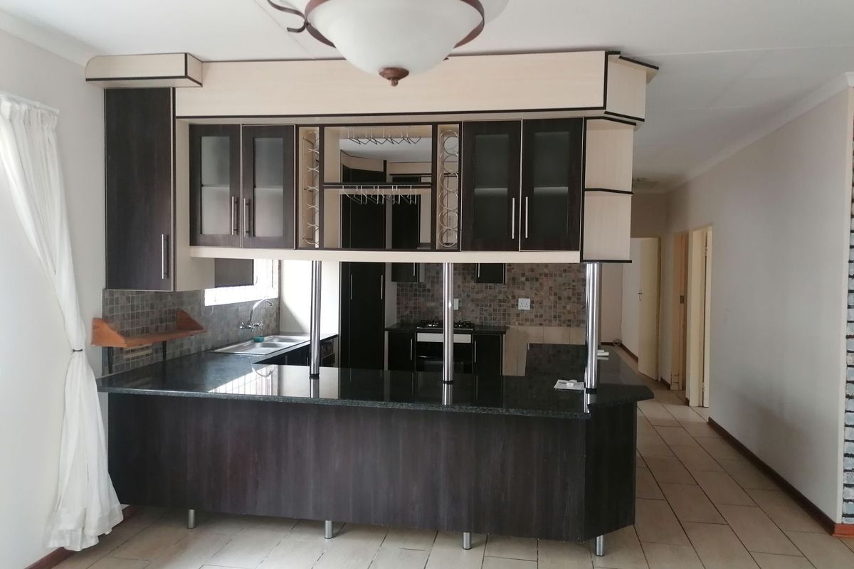 A functional kitchen featuring dark wood cabinetry, a granite breakfast bar, integrated wine glass storage, and a tiled backsplash.