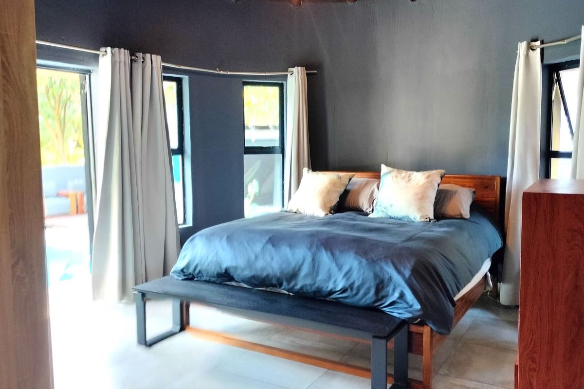A spacious bedroom featuring dark-toned walls, tiled flooring, and large windows that provide natural light and access to an outdoor area.