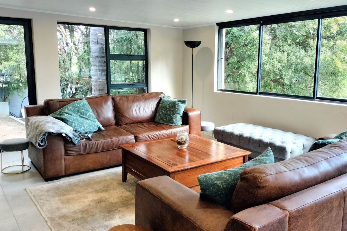 A bright and spacious living room featuring large windows with garden views, recessed ceiling lighting, and neutral tiled flooring.