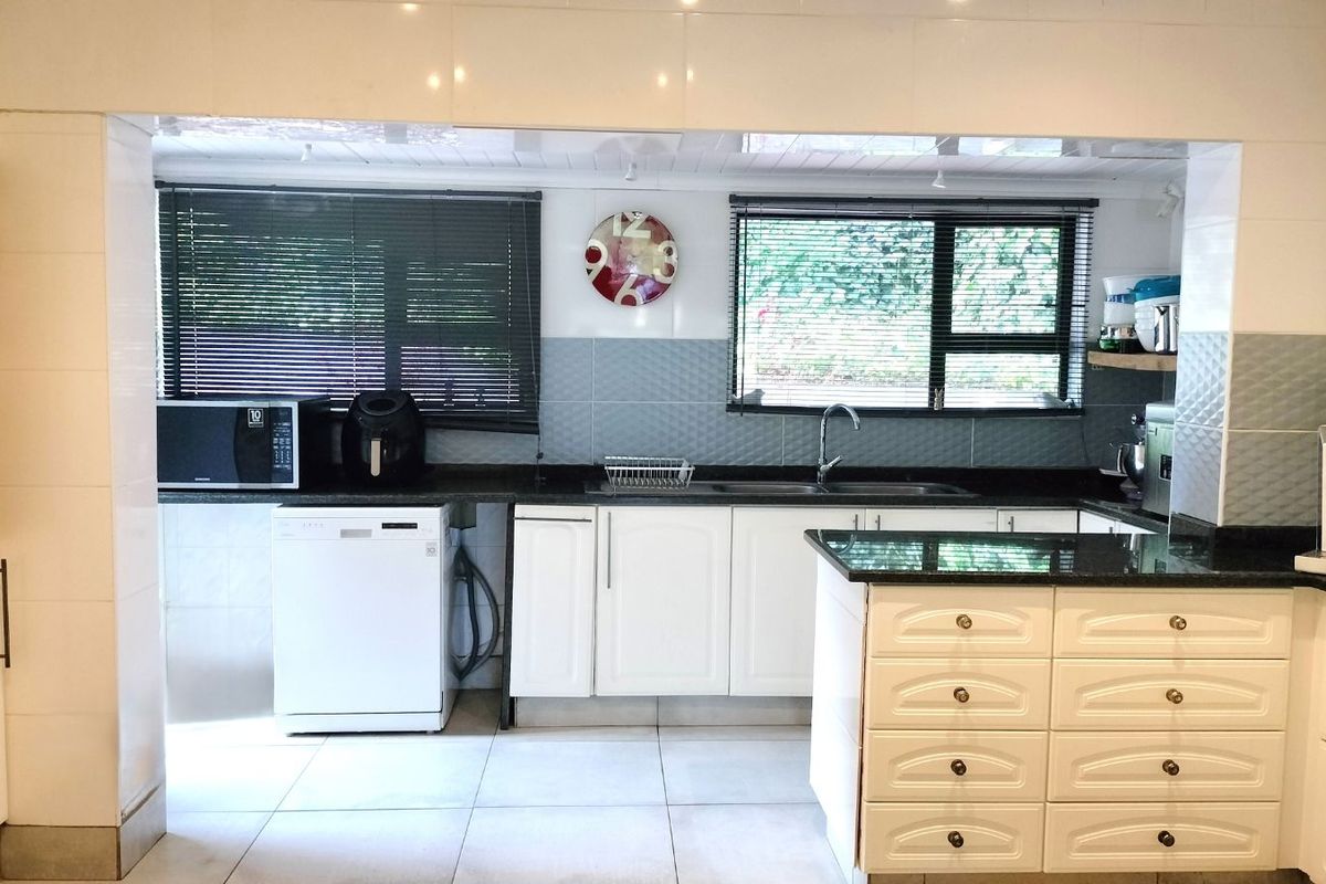 A functional kitchen featuring white cabinetry, dark granite countertops, tiled splashbacks, and a central island, providing ample workspace and storage.