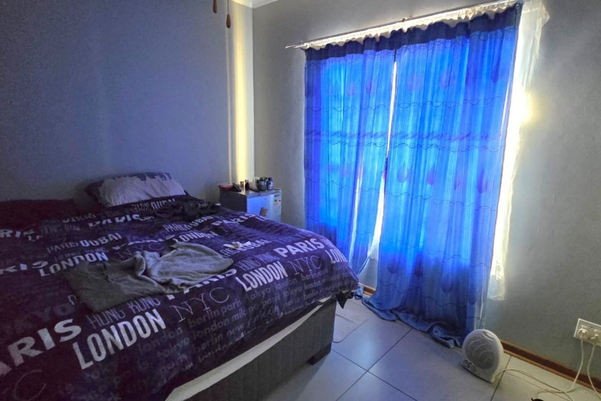 A bedroom featuring tiled flooring and large windows covered by curtains, providing natural light to the space.