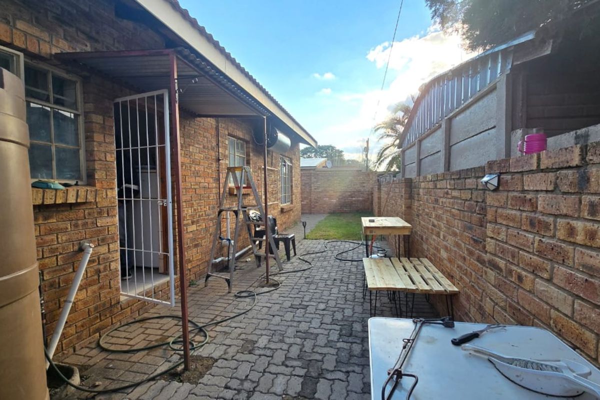 A side exterior area featuring brick paving, a brick boundary wall, and a metal security gate entrance to the townhouse.