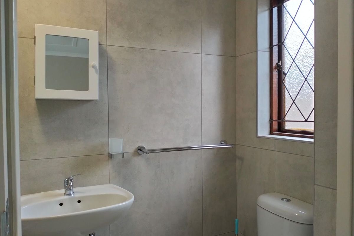 A clean, modern bathroom featuring large-format neutral wall tiles, a pedestal basin, a wall-mounted medicine cabinet, and a window with decorative leaded glass.