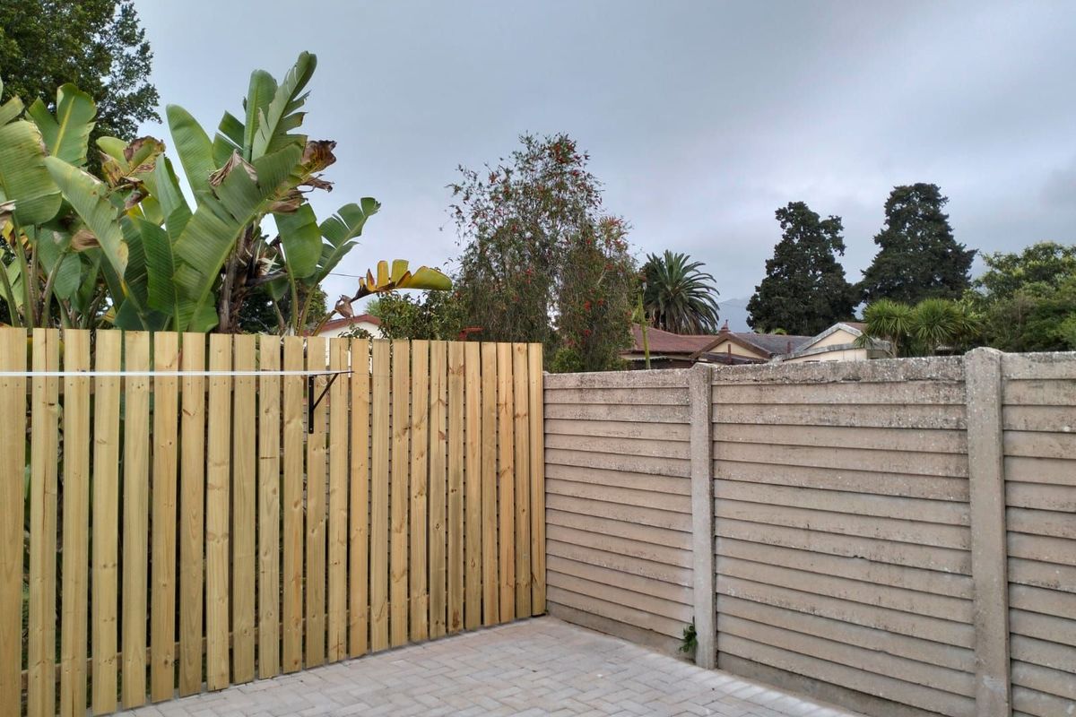 A private outdoor area featuring a new vertical timber slat fence, paved ground surface, and a concrete boundary wall with mature garden greenery.