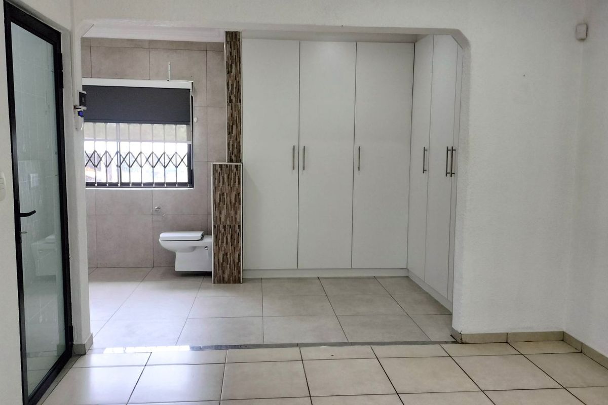 A clean, tiled bedroom area featuring built-in white cabinetry and an en-suite bathroom space with a wall-mounted toilet and security gate.