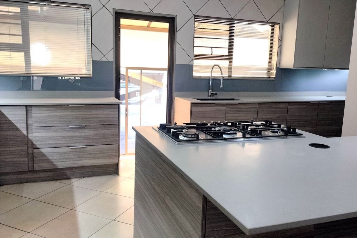 Modern kitchen featuring wood-grain cabinetry, stone countertops, a central island with a built-in gas hob, and tiled flooring.