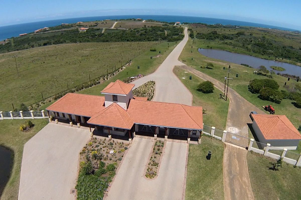 Aerial view of the residential estate entrance gatehouse, featuring tiled roofing, paved driveway access, and surrounding landscaped grounds with coastal views.