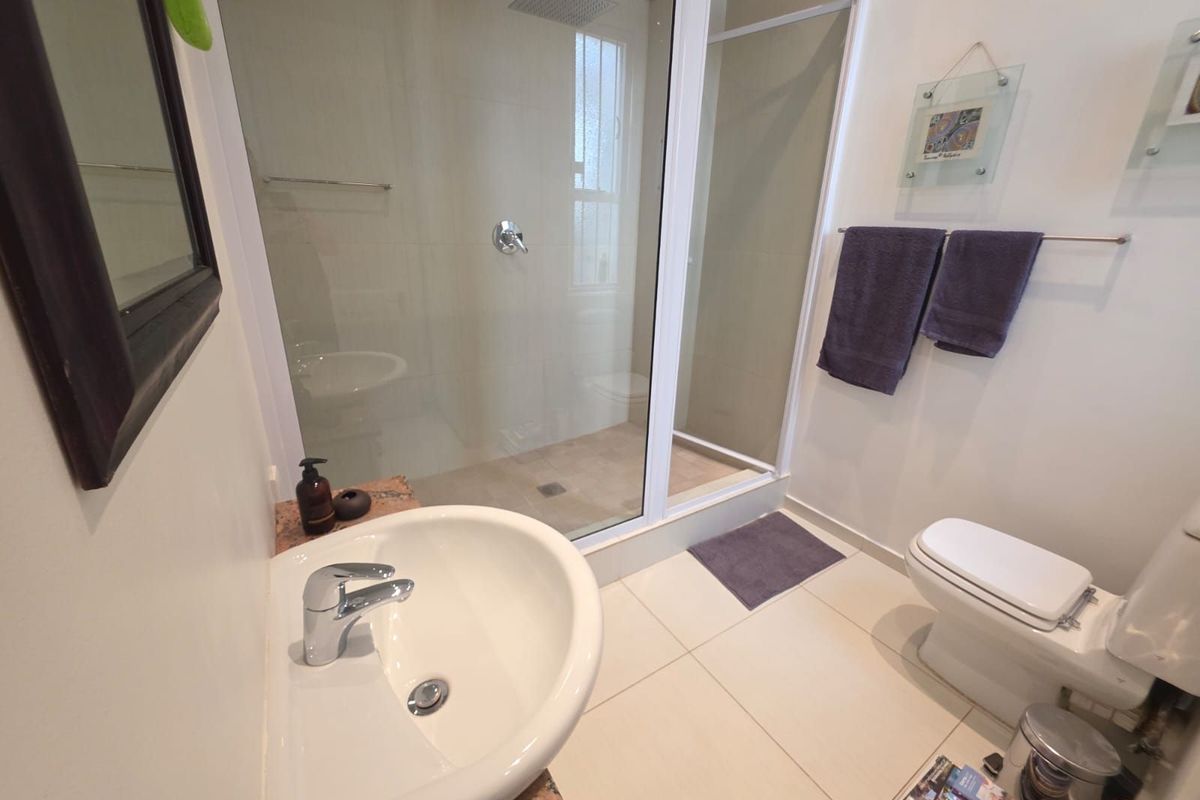A modern bathroom featuring a glass-enclosed walk-in shower with a rainfall showerhead, a pedestal basin, and a standard toilet.
