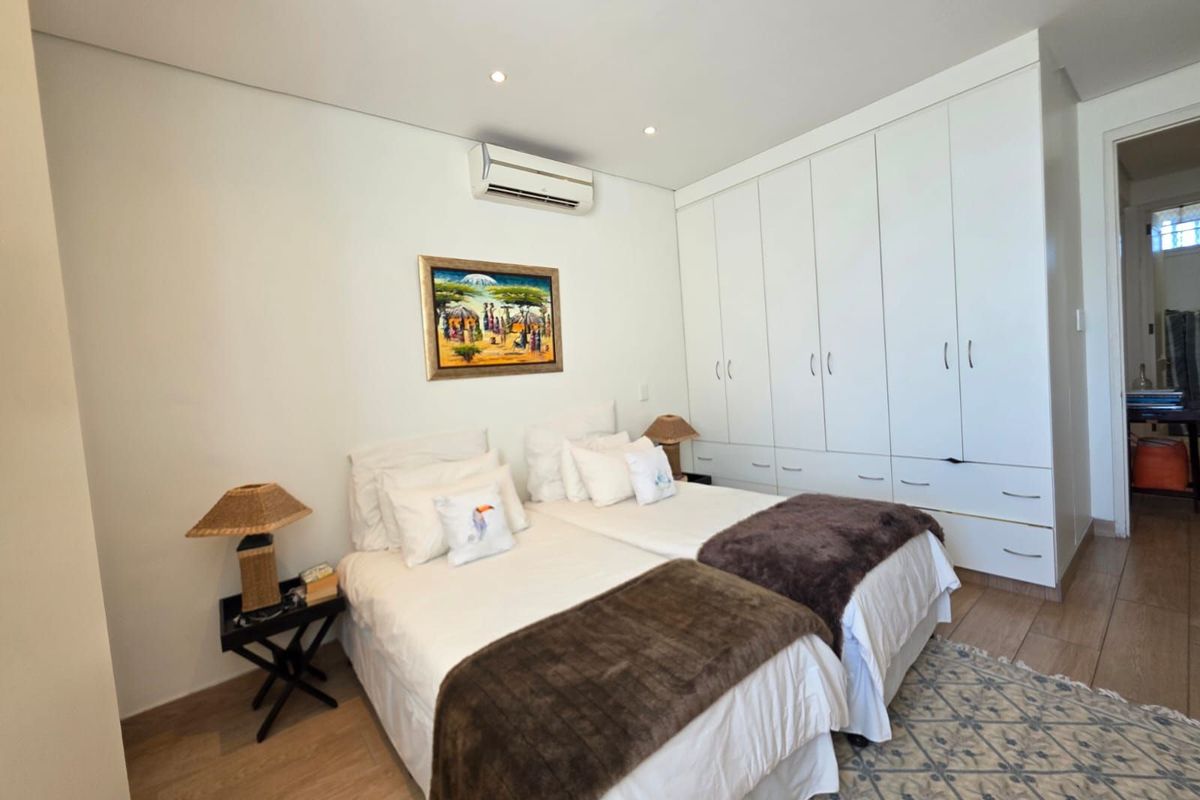 A well-maintained bedroom featuring built-in floor-to-ceiling wardrobes, recessed ceiling lighting, and a wall-mounted air conditioning unit with light wood-look flooring.
