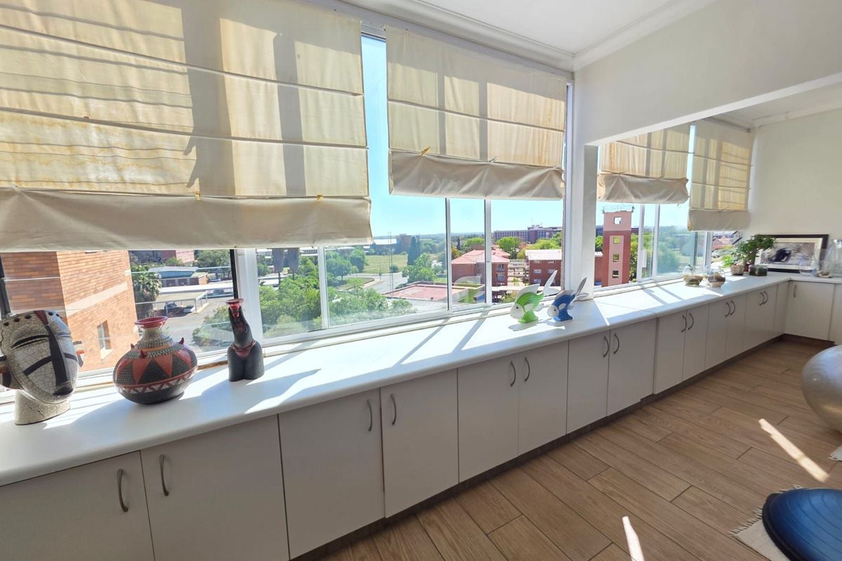 A bright living area featuring extensive built-in cabinetry along a large window wall, offering panoramic views and wood-look tiled flooring.