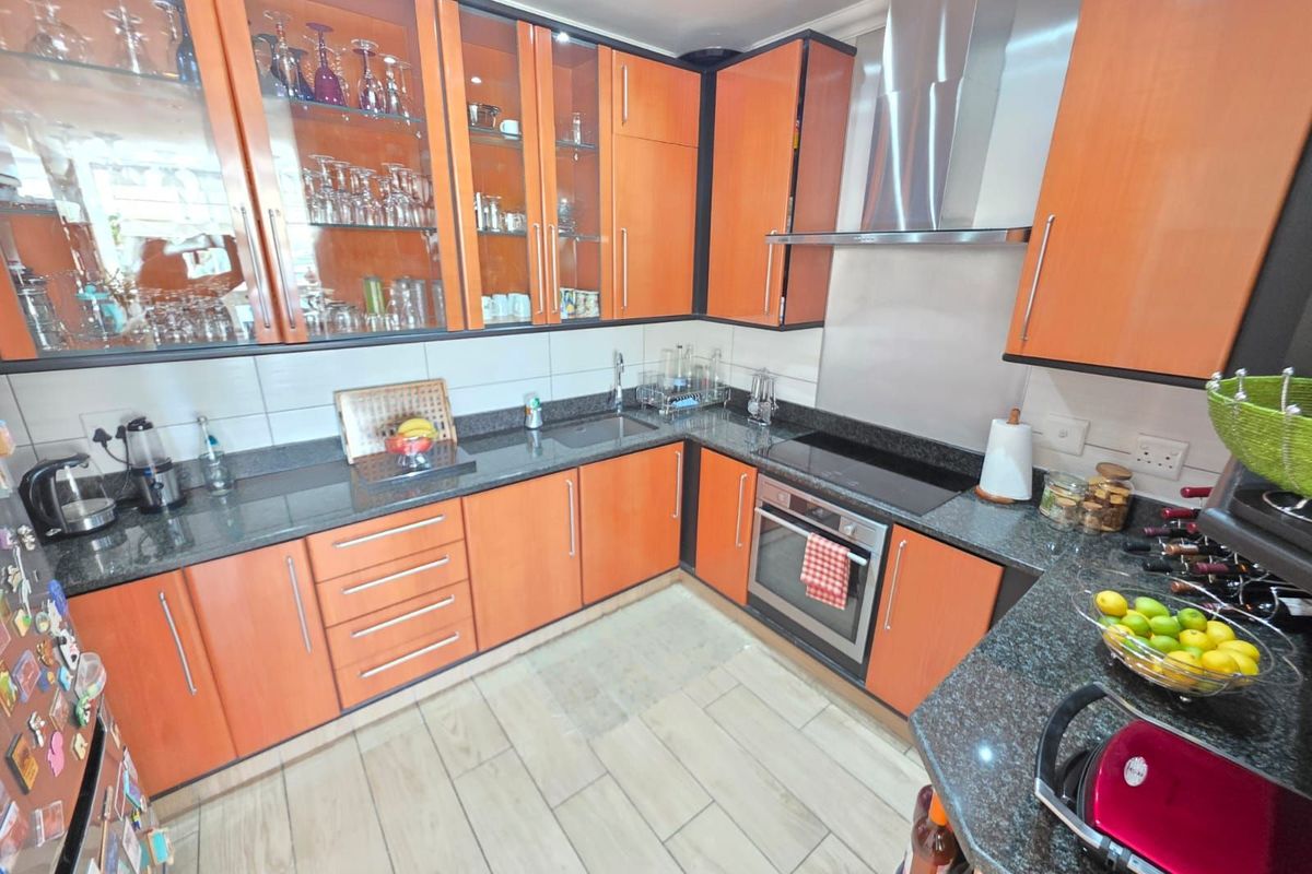 A functional kitchen featuring wood-finish cabinetry, dark granite countertops, a built-in oven, glass-top hob, and a stainless steel extractor fan.