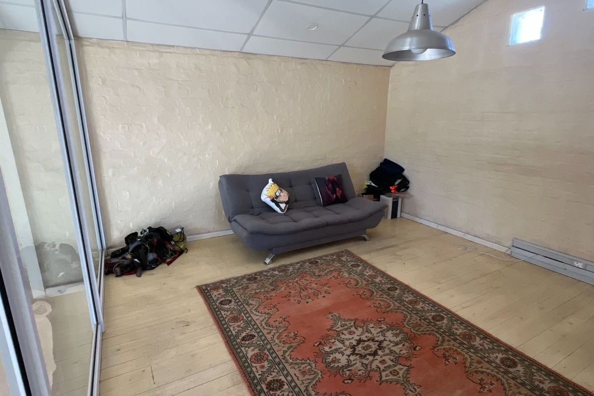 A simple industrial-style room featuring painted brick walls, a suspended ceiling, and light-toned timber flooring with a large pendant light fixture.
