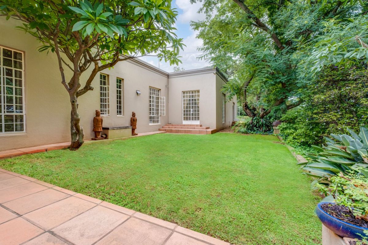A well-maintained rear garden featuring a manicured lawn, mature trees, and tiled patio area adjacent to the building's exterior facade.
