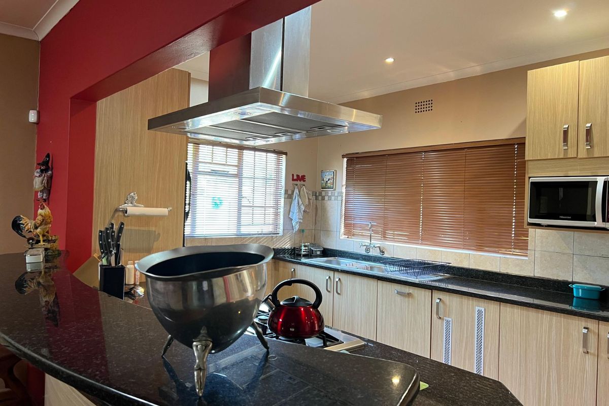 A functional kitchen featuring light wood-grain cabinetry, dark granite countertops, a stainless steel extractor fan, and a built-in microwave.