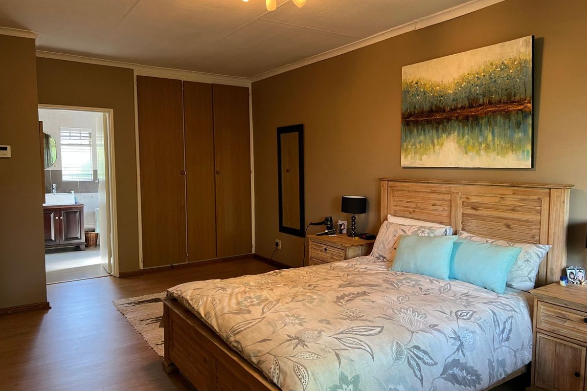 Spacious bedroom featuring built-in wooden cupboards and an en-suite bathroom with a vanity and window.