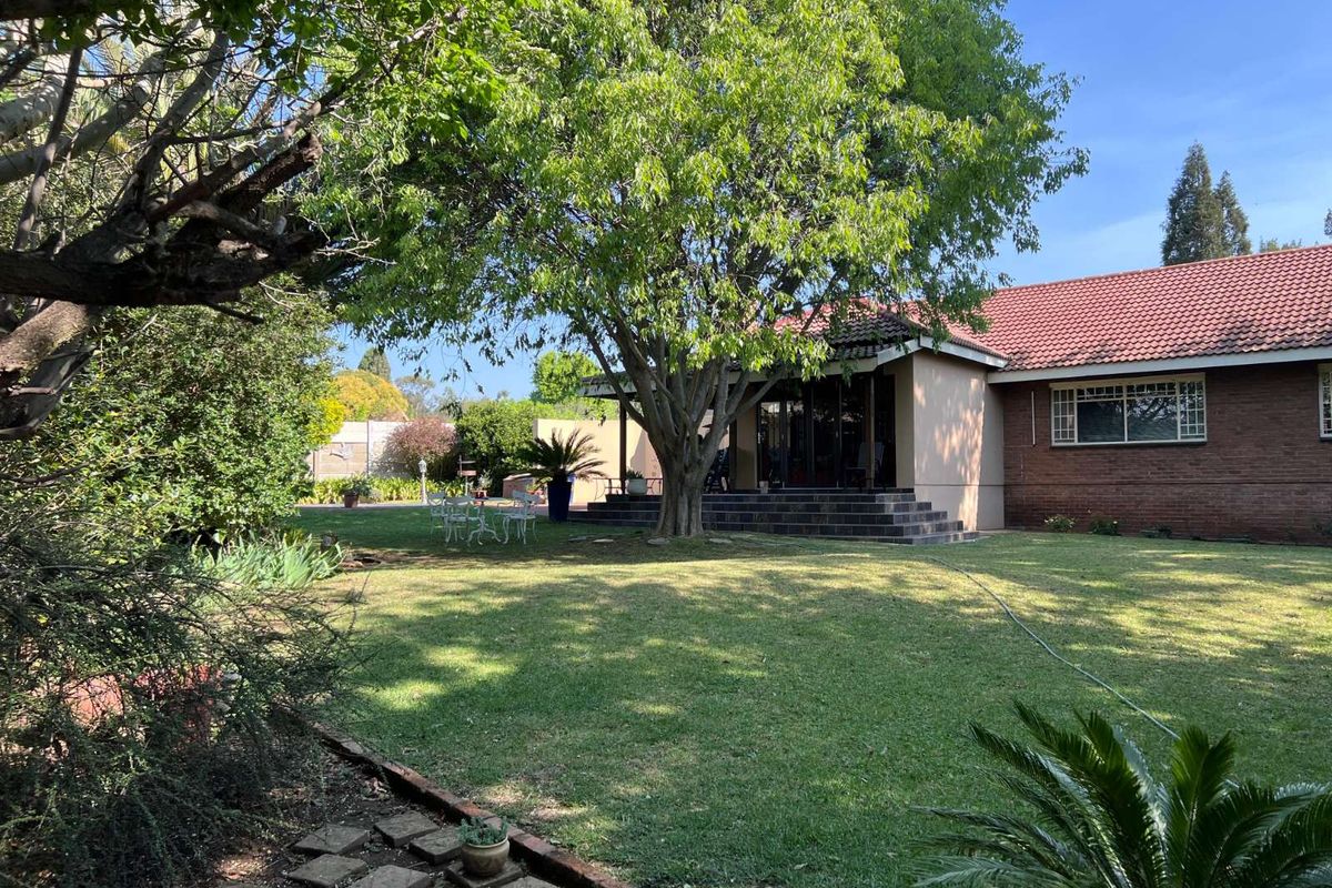 A view of the rear garden featuring a well-maintained lawn, mature trees, and a covered patio area attached to the brick-built house.