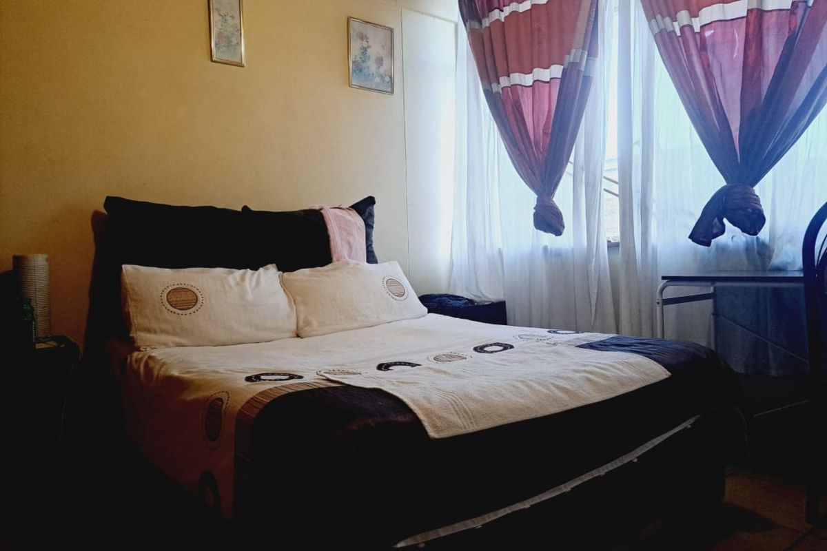A bedroom featuring a large window with natural light, neutral wall finishes, and tiled flooring.