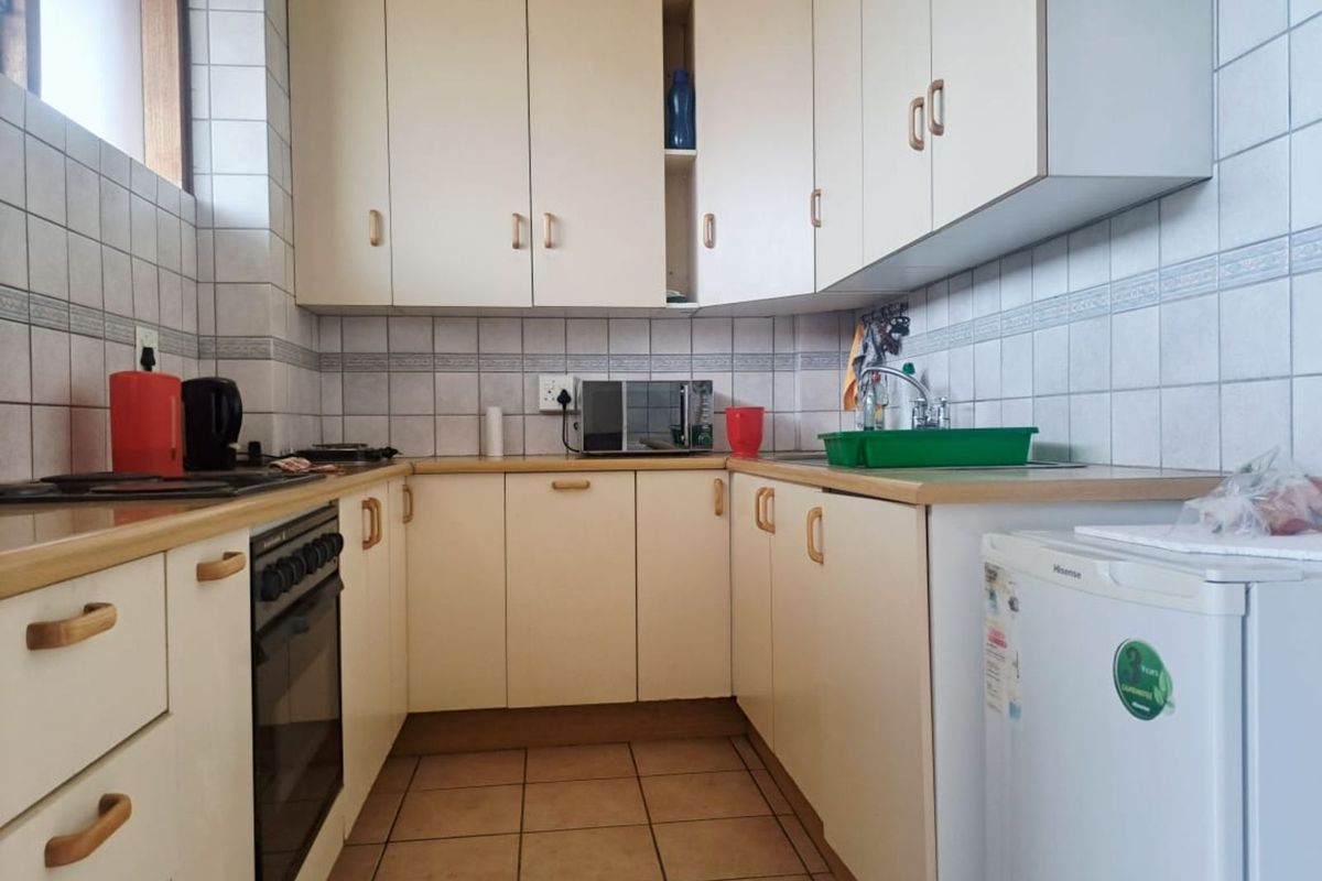 A compact kitchen featuring laminate countertops, built-in cabinetry, a fitted oven, and tiled splashbacks.