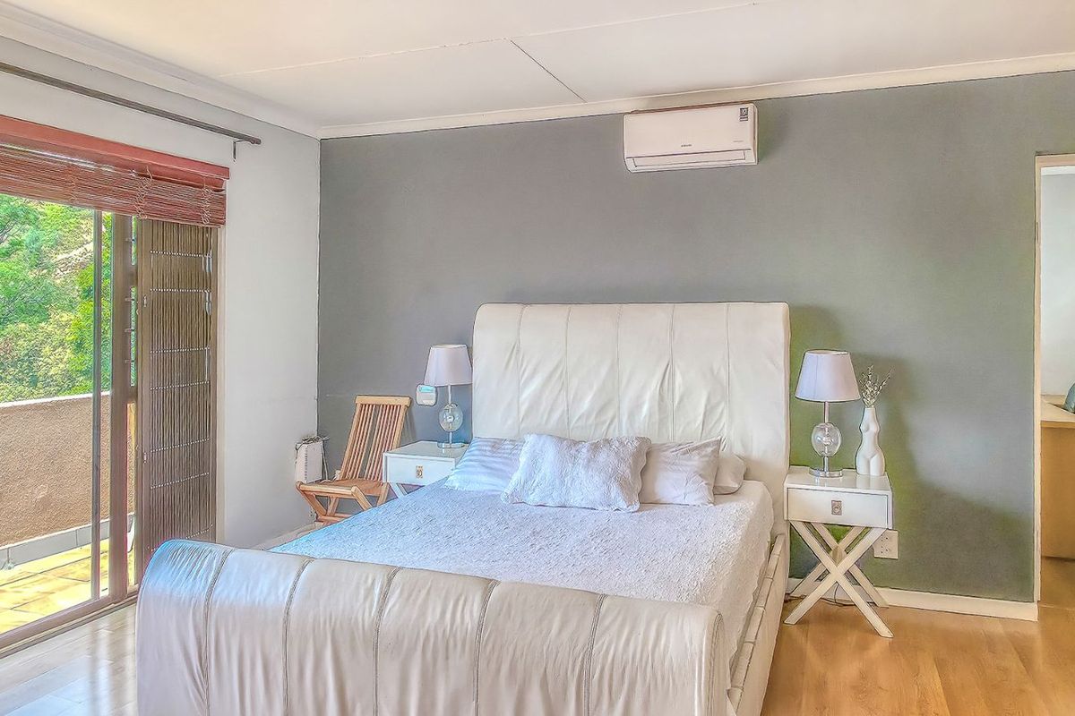 A well-lit bedroom featuring wood-look flooring, a wall-mounted air conditioning unit, and sliding glass doors providing access to an outdoor balcony area.