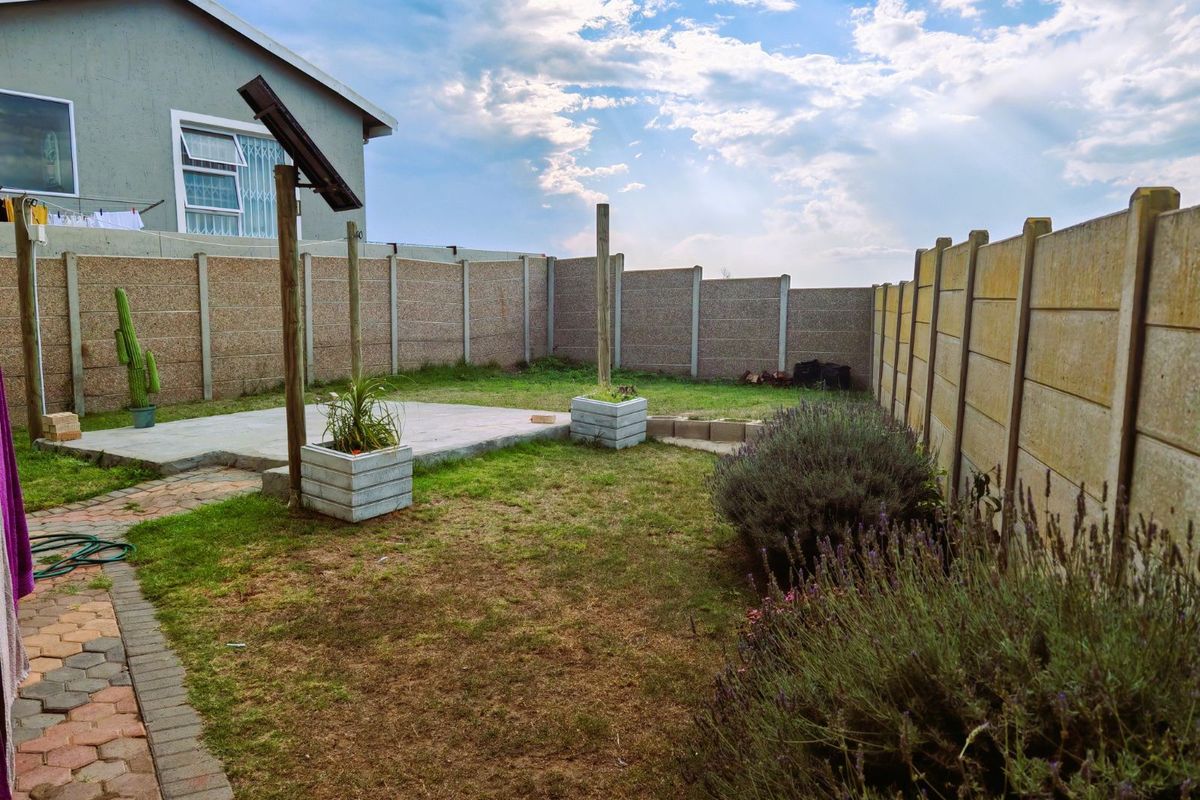 A private rear garden featuring a paved patio area, established garden beds, and secure perimeter walling.