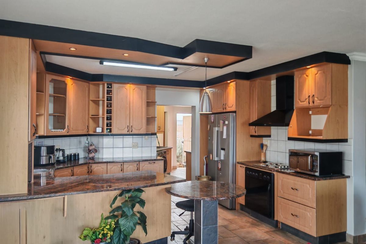 Spacious kitchen featuring light wood cabinetry, granite countertops, a built-in oven with extractor fan, and a breakfast nook, with an adjoining scullery area.