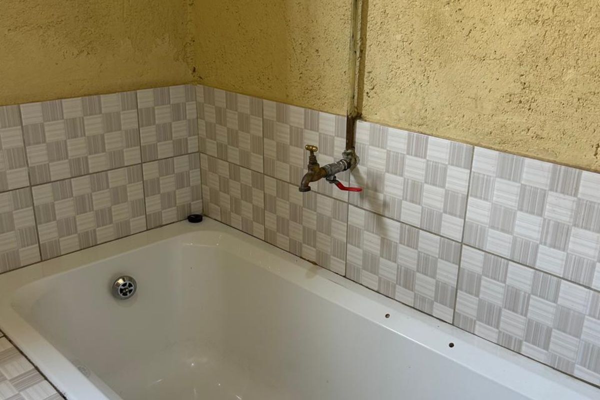 A bathroom area featuring a built-in bathtub with tiled surround and exposed plumbing fixtures against a textured wall finish.