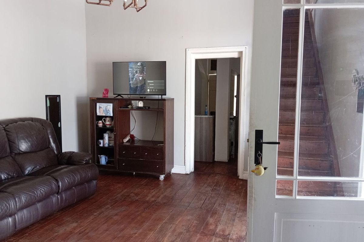 A living room featuring original timber flooring, a classic chandelier, and a doorway leading to an adjacent space with a staircase.