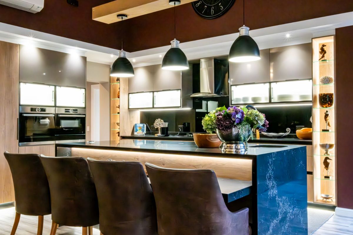 Modern kitchen featuring a large central island with stone countertop, integrated appliances, sleek cabinetry, and stylish pendant lighting.